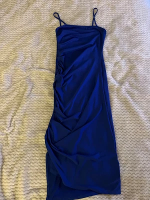 Marinblå långklänning med smala axelband - Säljer en stilren marinblå långklänning med smala axelband och lätt drapering på sidan. Klänningen har en figurnära passform och är tillverkad i ett mjukt, följsamt material som ger en snygg siluett. Perfekt för dig som vill ha en enkel men elegant look.