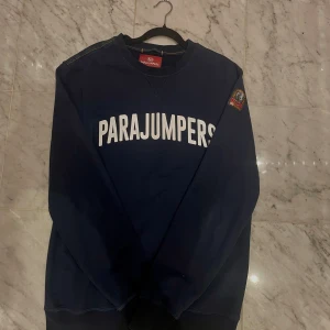 Mörkblå sweatshirt från Parajumpers - Snygg mörkblå sweatshirt från Parajumpers med stort vitt tryck över bröstet och patch på ena ärmen. Tröjan har rund hals och långa ärmar, perfekt för dig som gillar streetwear och vill ha en cool look. Obs, varan är falsk