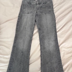 Grå bootcut jeans med fickor - Snygga grå jeans med bootcut passform och markerade sömmar längs benen. Framtill finns två stora fickor och baktill klassiska jeansfickor. Jeansen har en rak midja och är tillverkade i mjukt denim-material.