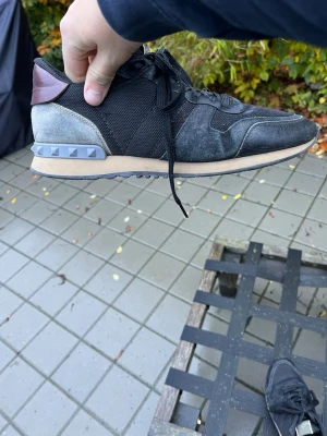 Valentino Garavani Rockrunner sneakers - Snygga Valentino Garavani Rockrunner sneakers i svart mesh och mocka med grå och vinröda detaljer. Skorna har coola nitar på hälen, snörning och platt sula. Perfekt för dig som vill ha en lyxig och unik sneaker med street vibe.