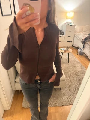 Brun kofta med dragkedja - Mörkbrun kofta med lång ärm och dragkedja hela vägen framtill. Modellen är figurnära med lätt utsvängda ärmslut och enkel, stilren design.