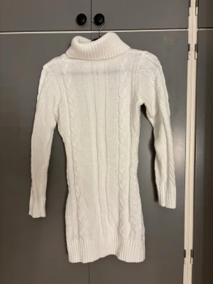 Vit stickad poloklänning med kabelmönster - Säljer en vit stickad poloklänning med snyggt kabelmönster och ribbade muddar. Tröjan har lång ärm och hög polokrage som ger extra mysfaktor. Perfekt för kyliga dagar och passar dig som gillar klassisk stil med en modern twist.