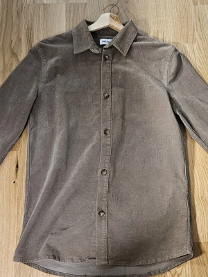 Beige manchester overshirt från Weekday - Snygg beige overshirt från Weekday i mjuk manchester. Funkar också som en vanlig lite tjockare skjorta. Klassisk skjortkrage, knäppning med knappar framtill och långa ärmar med knapp vid manschetten. Perfekt att slänga på över en t-shirt för en chill look.