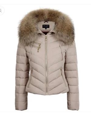 Äkta Beige jacka från Hollies Stockholm  - Knappt använd, snygg beige pufferjacka från Hollies med stor fluffig päls runt kragen. Jackan har guldiga dragkedjor, quiltad design och figurnära passform. 