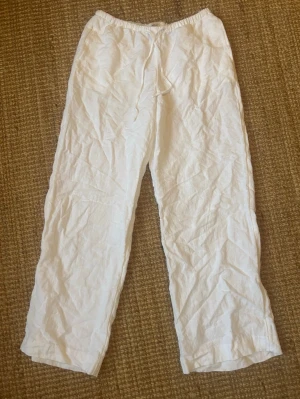 Vita linnebyxor med resår och snörning - Säljer ett par vita linnebyxor i storlek S. Byxorna har resår i midjan med snörning och en bakficka. De är raka i modellen och gjorda i en skön linneblandning, perfekta för varma dagar. Superlätta att matcha med en enkel t-shirt eller skjorta.