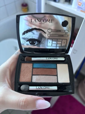 Lancôme ögonskuggspalett med borstar - Snygg ögonskuggspalett från Lancôme med fem nyanser: koppar, blå, beige, champagne och brun. Kommer i en svart kompakt dosa med spegel och två sminkborstar. Perfekt för att skapa olika ögonlooks med både matta och skimrande färger.
