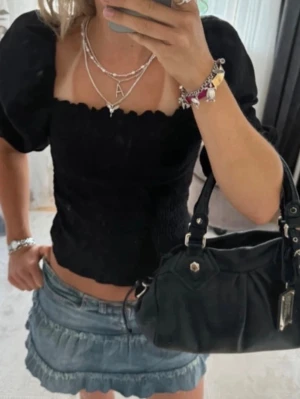Svart blus med puffärm från H&M - Säljer en svart blus från H&M i storlek S. Toppen har puffiga långärmar, fyrkantig halsringning och smockad, ribbad struktur. 