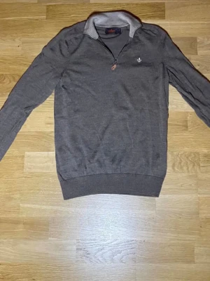 Grå långärmad tröja med half zip - Säljer en stilren grå pikétröja från Morris med lång ärm och half zip framtill. Tröjan har en klassisk krage i ljusare ton och Morris-logga broderad på bröstet. Perfekt till chill eller mer uppklädda tillfällen.