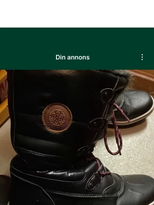 Svarta vinterstövlar med fuskpäls - Säljer ett par svarta vinterstövlar från Duffy med fuskpäls runt skaftet och vinröda snören. Stövlarna har en rund tå, platt sula och dekorativt märke på sidan. Perfekta för kalla dagar och har en robust yttersula för bra grepp. Säljs på fler sidor. Köparen betalar frakt.