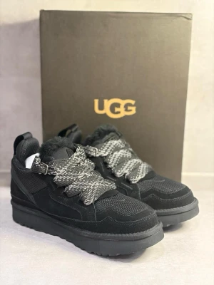 Svarta sneakers från UGG med päls - Säljer ett par svarta UGG sneakers med grov platt sula och breda snören i grått och svart mönster. Skorna har detaljer i mocka och mesh samt mjuk päls på insidan för extra komfort. Perfekt för dig som vill ha både stil och värme.