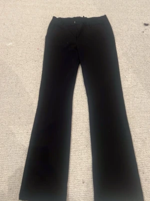 Svarta bootcut kostymbyxor - Snygga svarta kostymbyxor med bootcut-snitt och klassiska fickor fram. Byxorna har bälteshällor och är tillverkade i ett slätt material som ger en stilren look. Perfekta för dig som gillar en enkel men trendig stil.