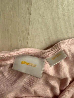 Ljusrosa topp med fyrkantig ringning - Supersöt ljusrosa topp från Gina Tricot med korta ärmar och snygg fyrkantig ringning. Toppen är i mjuk bomull och har en slim passform som sitter snyggt på kroppen. Perfekt att matcha med jeans eller kjol för en fräsch look.