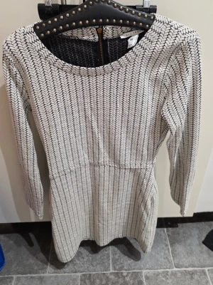 Vit och svart stickad klänning NLY Trend - Säljer en snygg stickad klänning från NLY Trend i storlek M. Klänningen är vit med svarta detaljer i ett coolt mönster, har lång ärm och dragkedja i ryggen. Passar perfekt för dig som gillar stilrena och bekväma plagg med lite edge.