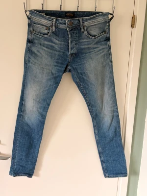 Blå skinny jeans från Jack & Jones - Pris går att diskuteras. Snygga blå jeans från Jack & Jones i skinny fit med klassisk femficksdesign och knappgylf. Jeansen har en tvättad look med ljusare partier och slitningar som ger en cool vibe. Perfekta för dig som gillar en smal siluett och vill ha ett stilrent plagg i garderoben.