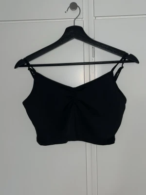 Svart croppad linnetopp  - Säljer en svart croppad linnetopp med smala axelband och lätt rynkning framtill. Toppen har en enkel och stilren design. Materialet känns mjukt och stretchigt, vilket gör den bekväm att bära under varma dagar. Har även justerbara band. Använd ett par gånger och är från SHEIN 