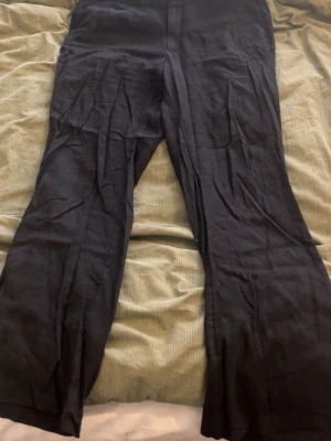 Linne kostymbyxor - Säljer ett par svarta linne kostymbyxor från H&M med raka ben och hög midja. Byxorna har diskreta bakfickor och stängs med dragkedja och hake framtill. Perfekta för en chill och stilren look.