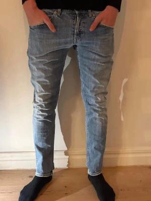 Dondup - Säljer ett par dondup  jeans i ljusblå tvätt med klassisk femficksdesign och smal passform. Jeansen har normal midja och raka ben, tillverkade i mjukt bomullsmaterial med lite stretch för extra komfort. Perfekt för dig som gillar en clean och stilren look.