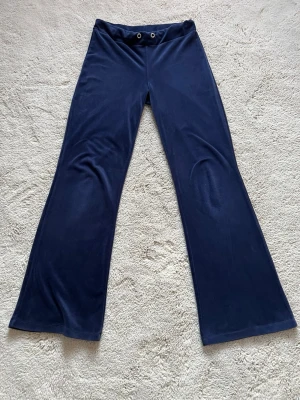 Mörkblå bootcut byxor från Gina Tricot - Snygga mörkblå bootcut byxor från Gina Tricot i mjukt och lent material. Byxornar har en bred linning med två metallöljetter framtill och är tillverkade i polyester. 