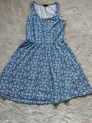 Blåvit mönstrad klänning - Säljer en blåvit kortklänning med ett snyggt geometriskt mönster. Klänningen är ärmlös och har rund halsringning. Passar perfekt om du ska åka utomlands. Passar personer som är Xs-M