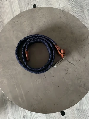 Mörkblå flätad bälte från Jack & Jones - Säljer ett snyggt blått flätat bälte från Jack & Jones med bruna skinn-detaljer och silvrigt spänne. Bältet har en cool struktur och passar perfekt till jeans eller chinos. Märket är präglat på läderdelen vid spännet. Längd: 80 cm. Köparen betalar för frakt