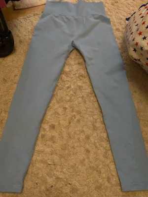 Ljusblå leggings i stretchig material - Säljer ett par ljusblå leggings med hög midja, perfekta för chill eller träning. De är gjorda i ett mjukt och stretchigt material med 60% polyamid, 30% polyester och 10% elastan. Sitter tight och följer kroppen snyggt.