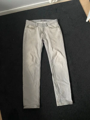 Grå jeans från Dressmann, storlek 29/32 - Säljer ett par gråa jeans från Dressmann i storlek 29/32. Klassisk femficksmodell med raka ben och normal passform. Jeansen har en ljusgrå ton Perfekt för dig som gillar stilrena och enkla jeans. 