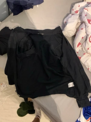 Svart långärmad overshirt i bomull - Svart hoodie från lager 157 i storlek M, tillverkad i mjuk bomull. Klassisk design med huva och långa ärmar, perfekt för chill dagar. Tröjan har ribbade muddar vid ärmslut och nederkant för extra komfort. Snygg och enkel att matcha med jeans eller joggers. Priset kan sänkas vid snabb affär!