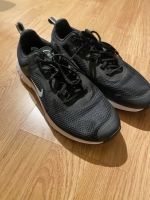 Svarta Nike sneakers med snörning - Säljer ett par svarta Nike sneakers med vit sula och klassisk swoosh på sidan. Skorna har mesh-överdel för bra ventilation och snörning framtill. Perfekta för dig som gillar sportig stil och vill ha bekväma skor till vardags.