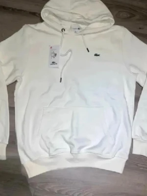 Lacoste Hoodie  - Säljer denna stilrena, nya och riktigt snygga vita Lacoste hoodien, passar perfekt till allt, dock är den liten i storleken, står XL men passar (M-L), skriv gärna vid intresse och för mer information!