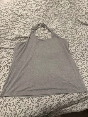 Grå ärmlös linnetopp - Säljer en enkel och stilren grå linnetopp med halterneck och ärmlös design. Toppen har en mjuk och slät yta, perfekt för varma dagar eller som layering-piece. Passar dig som gillar minimalistisk stil och vill ha något lätt och bekvämt.