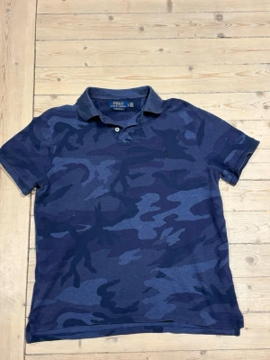  Ralph Lauren pike - Säljer en mörkblå pikétröja från Polo Ralph Lauren med coolt camouflage-mönster. Storlek är Large men den har krympt i tvätten, den sitter som small. Modellen är 181cm och väger 65
