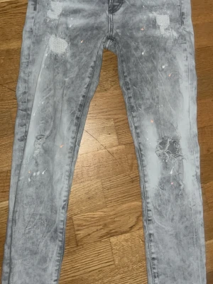 Dsquared2 skinny jeans i grått - Säljer ett par Dsquared2 skinny jeans i grå tvättad färg med slitna detaljer och färgstänk. Modellen är 71630 och har klassisk femficksdesign, knappgylf och Dsquared2-röd etikett. Jeansen är tillverkade i Italien och har en cool, modern look.