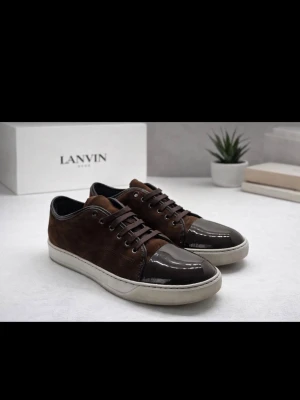 Bruna sneakers från Lanvin med lackad tå - Snygga bruna sneakers från Lanvin med ovandel i mocka och en glansig, lackad tå i mörkgrått. Skorna har snörning och vit platt sula som ger en clean look. Perfekta för dig som gillar stilrena detaljer och exklusiva material. Priser kan diskuteras, flera bilder kan skickas. GLÖM INTE ATT STÄLLA FRÅGOR!