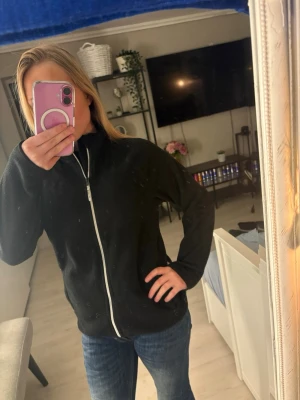 Svart fleecejacka med dragkedja - Svart fleecejacka med hel dragkedja framtill och hög krage. Jackan har en enkel och stilren design med två fickor på sidorna. Perfekt för lager-på-lager och passar till både jeans och träningsbyxor. 