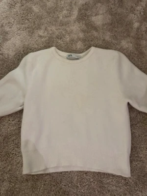 Vit stickad tröja från Zara - Säljer en enkel och stilren vit stickad tröja från Zara. Tröjan har rund halsringning och långa ärmar med ribbade muddar vid ärmslut och nederkant. Perfekt för lager-på-lager under kyliga dagar.
