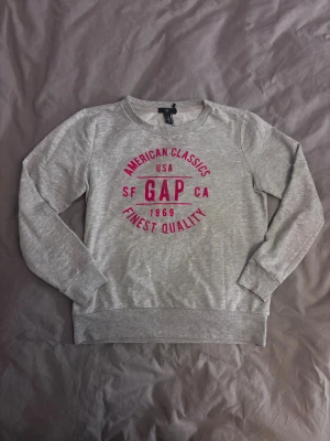 Grå sweatshirt från GAP med rosa tryck - Snygg grå sweatshirt från GAP med rosa tryck. Storlek S, men passar även XS. Köpt secondhand men aldrig använt själv. Fint skick på tröjan!!!🥰🥰💘💘💘
