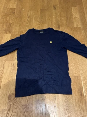 Marinblå stickad tröja Lyle & Scott - Säljer en marinblå stickad tröja från Lyle & Scott Junior med klassisk gul logga på bröstet. Tröjan har rund halsringning, ribbade muddar och lång ärm. Perfekt för dig som gillar stilrena och tidlösa plagg. Pris kan diskuteras.
