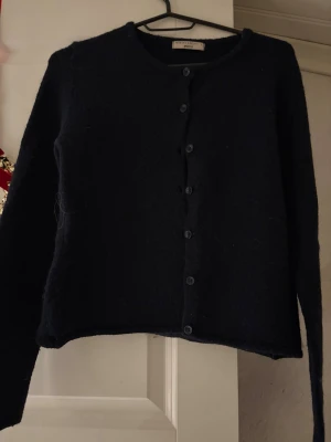 Marinblå kofta från Gina Tricot - Mysig mörkblå kofta från Gina Tricot med rund hals och knappar hela vägen framtill. Koftan har lång ärm och är tillverkad i ett mjukt stickat material som passar perfekt för kyliga dagar. Enkel och stilren design som är lätt att matcha.