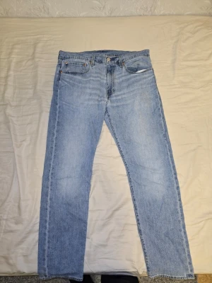 Levi's 501 ljusblå jeans straight fit - Ljusblå Levi's 501 jeans med klassisk femficksdesign och raka ben. Jeansen har en ikonisk läderpatch bak och knappgylf. Tillverkade i slitstarkt bomullsjeansmaterial med en avslappnad straight passform. Perfekt för dig som gillar tidlös denimstil. En defekt.