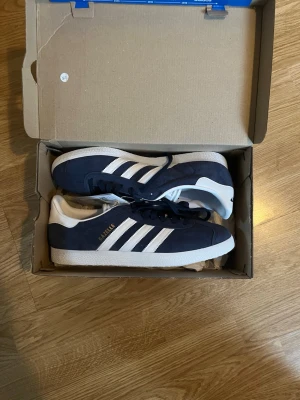 Adidas Gazelle marinblå sneakers - Säljer ett par klassiska Adidas Gazelle sneakers i marinblå mocka. Helt oanvända, stl 42 2/3. Ny pris 1349kr