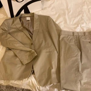 Beige kostym från Bläck, storlek 54 - Säljer en stilren beige kostym från Bläck i storlek M. Kostymen består av en klassisk kavaj med smala slag och matchande byxor med pressveck. Passar dig som gillar en clean och modern look. Knappt använd, då den är förstor, har tyvärr ingen modell på bilden.