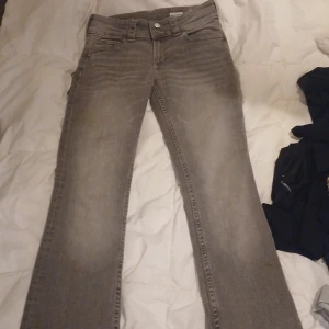 Grå bootcut jeans från H&M - Snygga grå bootcut jeans från H&M med låg midja och justerbar midja. Klassisk femficksmodell med en ficka bak som har lock och knapp. Jeansen har en cool tvättad look och är perfekta för dig som gillar avslappnad stil.