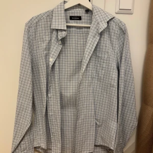 Rutig skjorta från Dressmann M - Klassisk rutig skjorta från Dressmann i vitt och blått. Skjortan har lång ärm, knappar framtill och en snygg krage. Perfekt för dig som gillar stilrena och tidlösa plagg. Tillverkad i mjuk bomull för en skön känsla hela dagen.