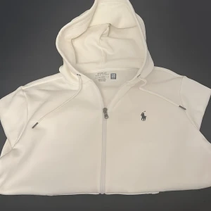 Vit hoodie från Polo Ralph Lauren - Vit hoodie från Polo Ralph Lauren i storlek M. Väldigt skön att ha på sig i vardagen och väldigt nice passform. Köpte tröjan för 2400kr nypris och säljer den nu för 1699kr pris kan diskuteras!!