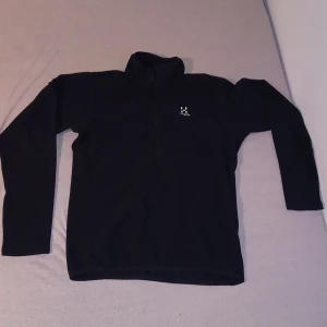 BLACK fleece-tröja HAGLÖFS (S) - BLACK fleece-tröja av Haglöfs i storlek S. Tröjan har hög krage, half zip-dragkedja och diskret Haglöfs-logga på bröstet. Perfekt för kyliga dagar och outdoor-aktiviteter. Mjuk och skön polyesterfleece med lång ärm.