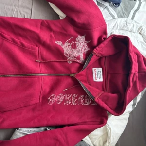 Vin röd laviago hoodie  - Säljer en cool röd hoodie från laviago med dragkedja och ett unikt mönster. Perfekt för en avslappnad stil med en touch av bling. Den har en bekväm passform och en praktisk huva. Storlek m men passar bra till dem som vanligt viss har s
