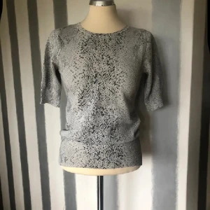 Glittrig silver stickad topp - Snygg stickad topp i silver med glittrigt material och ett coolt prickigt mönster. Rund halsringning och halvkort ärm ger en chill vibe. Perfekt för dig som gillar att sticka ut med lite extra shine.