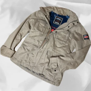 Field Jacket Superdry - Riksfet field jacket från Superdry i storlek Medium, sitter TTS – enkel att matcha och skön att bära. Ett stilrent val, noggrant utvalt med omsorg av AM Clothing.  📩 Frågor? Hör gärna av dig! 📲 Följ oss här på Plick för fler uppdateringar. ♻️ Tack för att du handlar mer hållbart med AM Clothing!