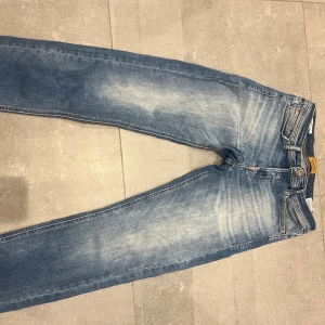 Blå jeans från Jack & Jones - Snygga blå jeans från Jack & Jones med slitna detaljer och klassisk femficksdesign. Jeansen har normal passform och är tillverkade i bomull med en tvättad look. Perfekta för en avslappnad stil.
