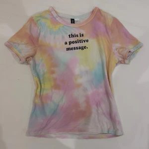 Pastell tie-dye t-shirt från DIVIDED - Säljer en kortärmad t-shirt från DIVIDED i storlek S med färgglatt tie-dye mönster i pastelltoner. Tryck på bröstet med texten 'this is a positive message'. Mjuk och skön bomullskvalitet, perfekt för dig som gillar färg och statement-plagg.
